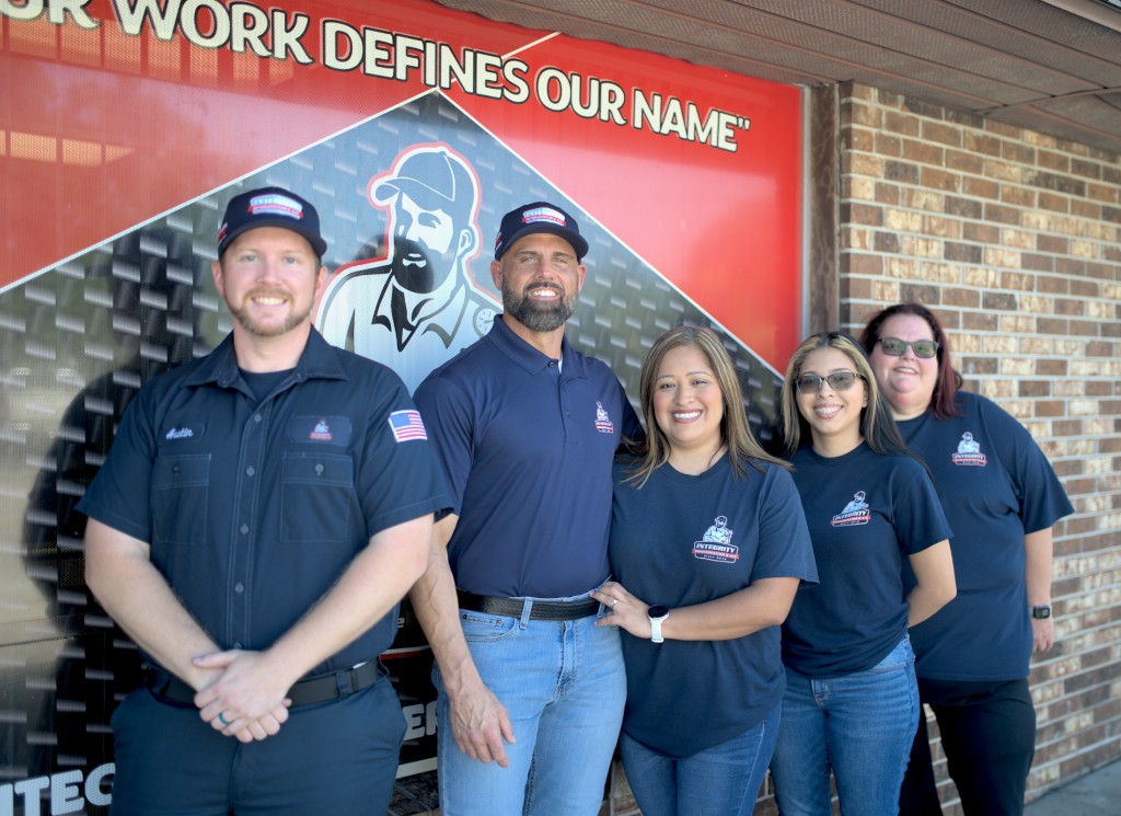 Integrity Refrigeration & AC team smiling outside their storefront beneath the "Our Work Defines Our Name" sign