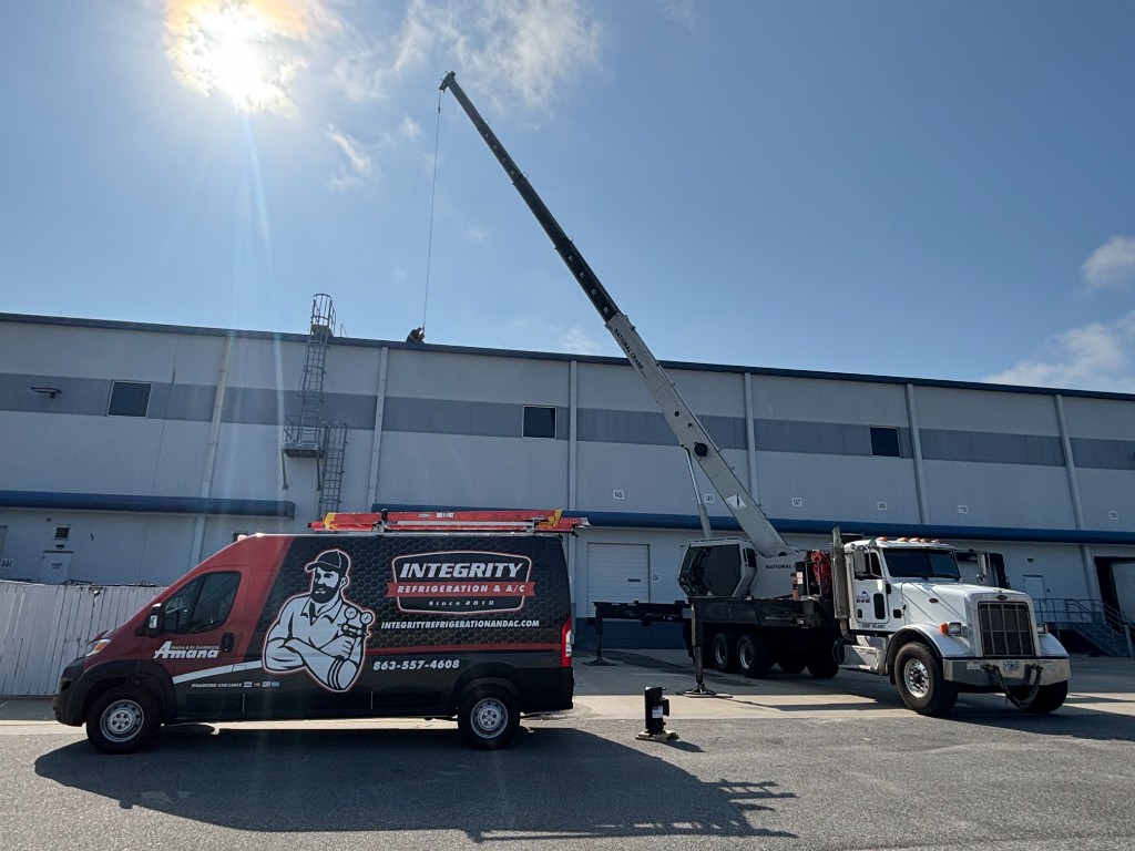 Integrity Refrigeration & AC branded service van and crane truck at a commercial HVAC job site